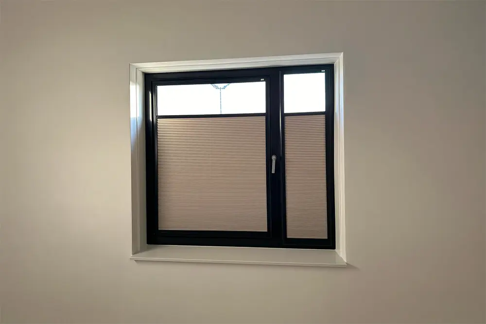 Verduisterend plisségordijn in beige op een raam met zwart kozijn